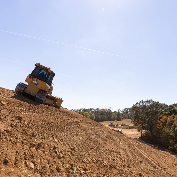 Bulldozer moving at an angle over a dirt hill with a treeline in the distance.